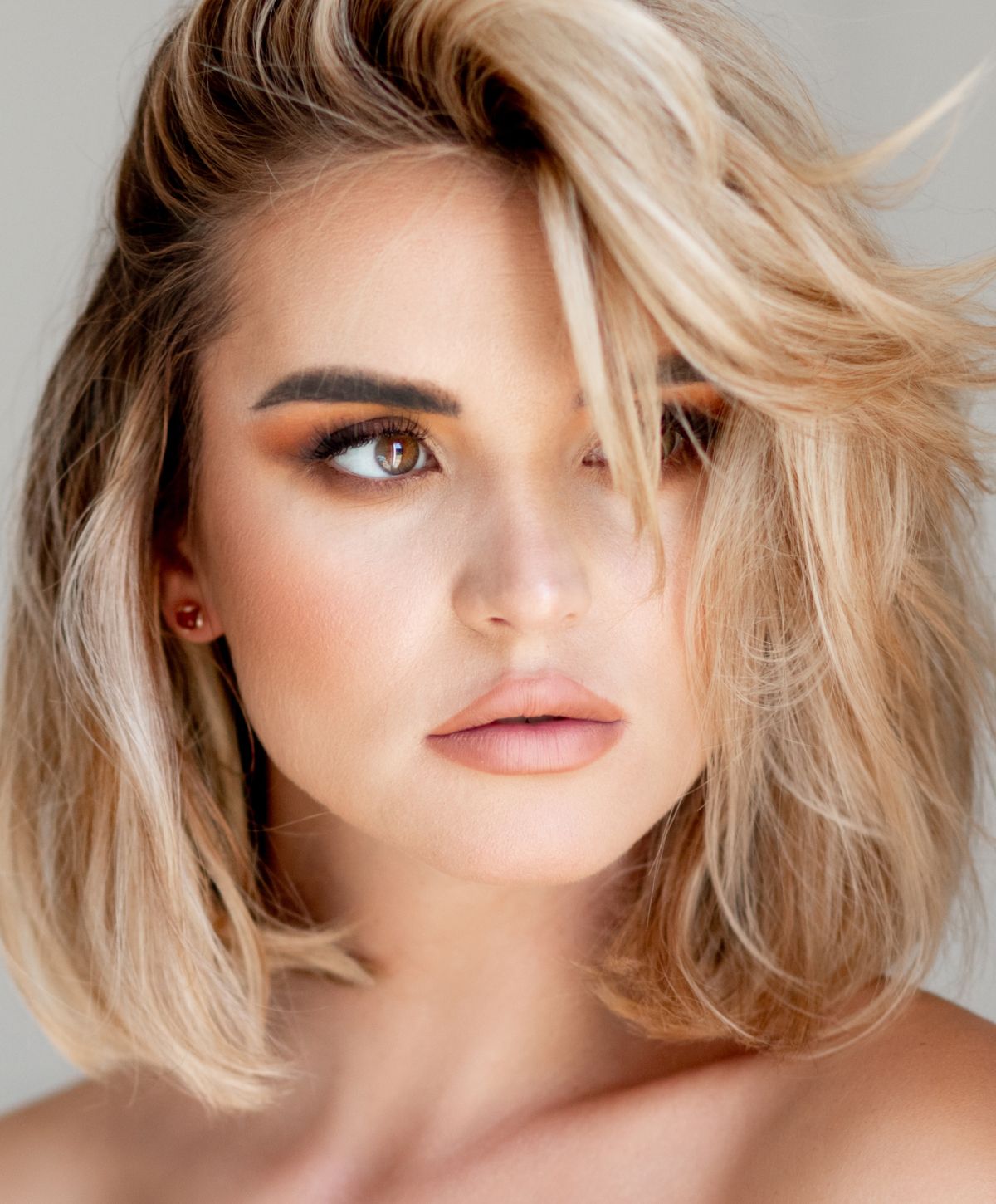 Dedham lip filler model with earrings among soft, blurred wheat.